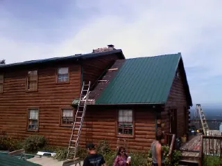 Green metal roof going on a two story log home with ladders set in Newton