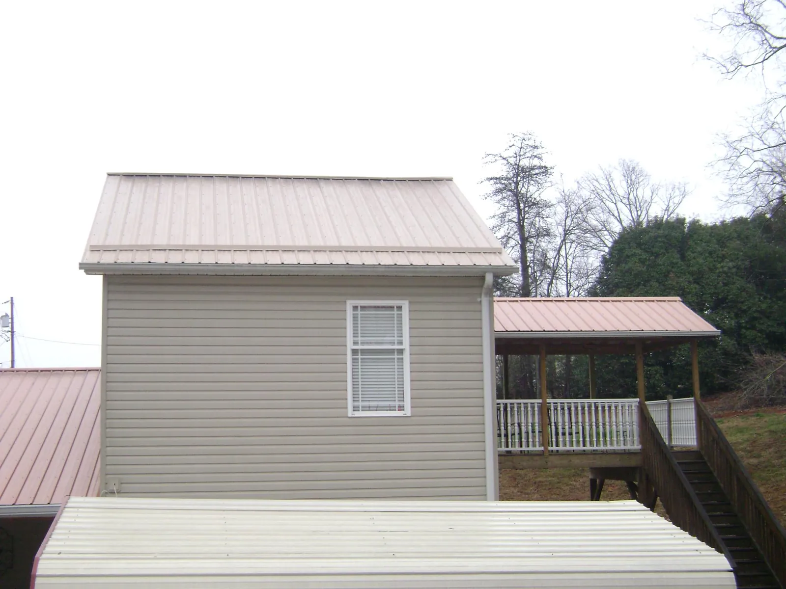 Tan metal roofs on a two story addition and attached porch, from a Roof Replacement job in Newton